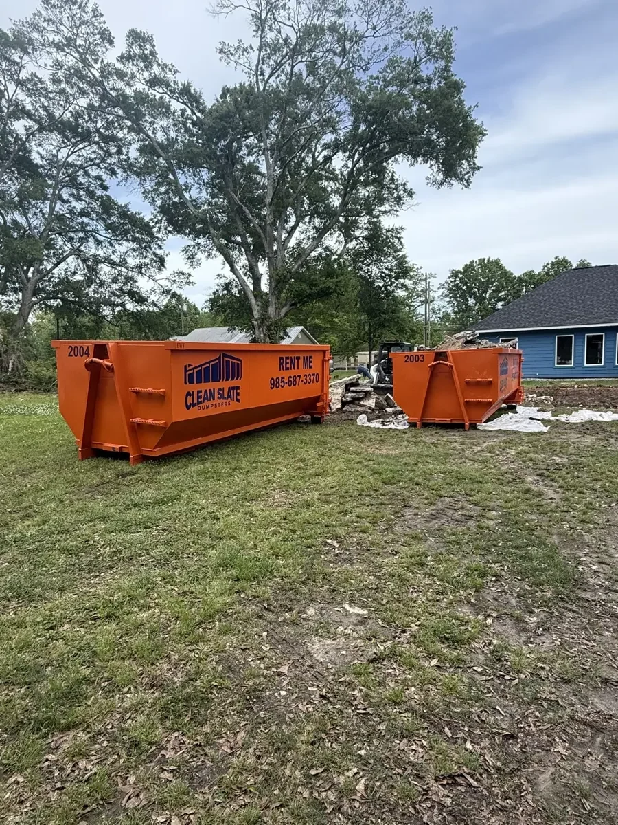 Two orange Clean Slate roll-off dumpsters set on a residential build site, one loaded with debris