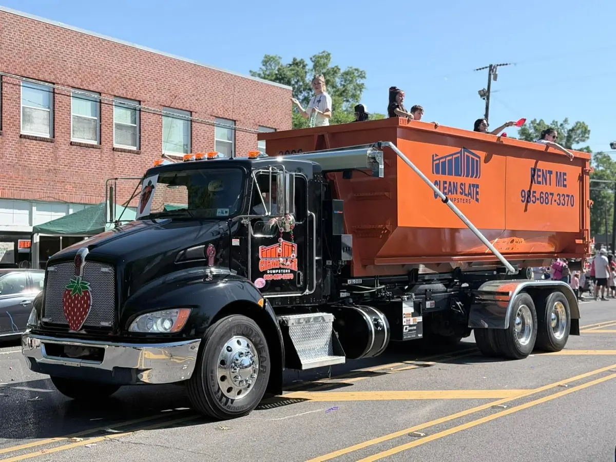Clean Slate Dumpsters roll-off truck with a strawberry-decaled grille and an orange dumpster in the Ponchatoula Strawberry Festival parade